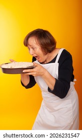 Housewife With Homemade Cakes On A Colored Background.
Shot Of Joyful Positive Mature Woman Enjoying Birthday Party Eating Apple Pie. Senior Woman Posing With Dessert. Celebration, Food And Dessert.