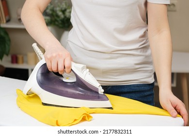 A housewife irons a yellow T-shirt with an iron. Ironing clothes at home, caring for clothes. Hands close-up