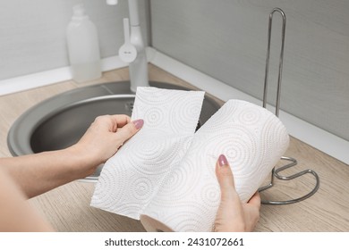 housewife in the kitchen tears off a paper towel. paper towel holder. using a paper towel. hand tears off a piece of paper towel.