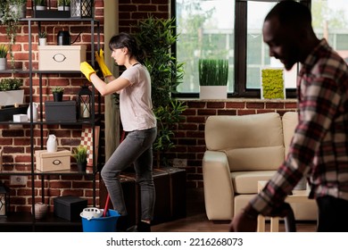 Housewife Moving Heavy Shelves At Home African American Husband Helps Vacuuming Floor. Multiracial Couple Doing Spring Cleaning, Moving Furniture Around To Give The Apartment A New Style.