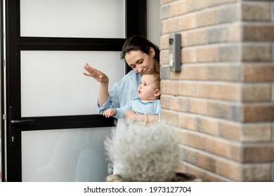 Housewife With Newborn Baby Staying In Front Of Entrance Door And Waving Goodbye To Husband And Dad Who Going To Work. Family Lifestyle. 