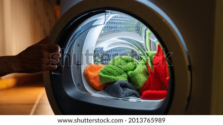 Housewife opens a  washing machine or dryer at night with many colorful clean fresh hand towels