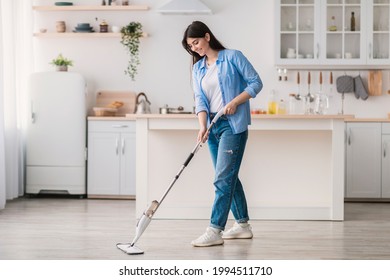 Housewife. Portrait of casual woman washing hardwood laminate flooring using water spray mop pad and refillable bottle with cleaning agent. Blurred Kitchen Background, Free Copy Space, Modern Interior