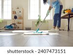 Housewife or professional cleaner mopping the floor at home. Crop young woman in an apron and gloves washing light gray wooden or laminate flooring in the living room. Housework, cleaning concept