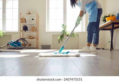 Housewife or professional cleaner mopping the floor at home. Crop young woman in an apron and gloves washing light gray wooden or laminate flooring in the living room. Housework, cleaning concept