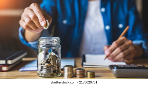 Housewife Puts A Coin In A Jar To Save Money For The Future. After Retirement And Record Keeping Of Income, Expenditure, Savings And Financial Concepts.