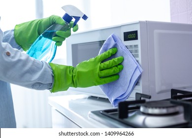 Housewife In Rubber Gloves Using Blue Rag And Cleaning Spray For Polishing And Washing Dirty Microwave Oven 