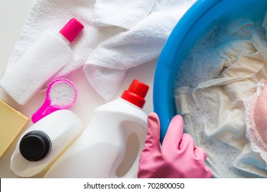 Housewife with rubber protective gloves washing clothes with different detergents in the bowl. Dry cleaning concept. Clothes care. Chores of maid. Regular washing. 