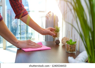 A housewife in a shirt is cleaning the house, wipes dust from the table with a cleaning rag. Household chores - Shutterstock ID 1240534453