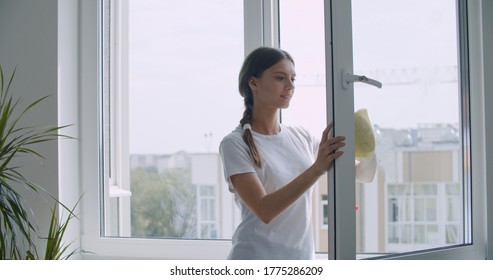 Housewife Sprays The Detergent On The Window And Wipes The Window With A Clean Microfiber Cloth. Clean Transparent Windows Without Streaks. Woman Cleaning House Concept