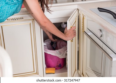 Housewife Throwing Out Garbage In The Kitchen Opening A Cupboard Door Under The Sink To Toss Waste Into The Bin As She Does The Cooking