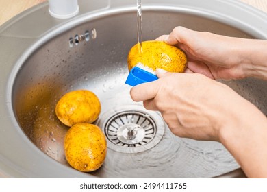 housewife washes fresh potatoes in the kitchen sink. washing potatoes in the kitchen. peeling potatoes.  - Powered by Shutterstock