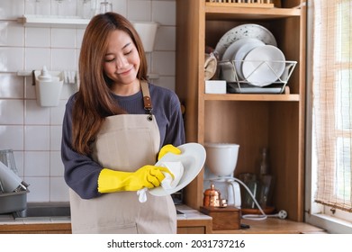A housewife wearing apron and protective glove, cleaning and washing dishes in the kitchen at home