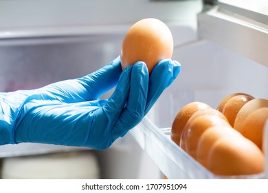 Housewife Wearing Blue Latex Gloves Stocking Fresh Chicken Eggs In Refrigerator. People Panic And Prepare To Pandemic Quarantine. Stay At Home Policy From Government During Coronavirus Or COVID-19