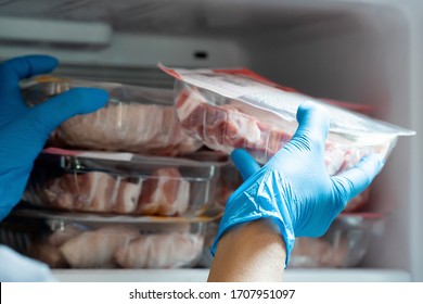 Housewife Wearing Blue Latex Gloves Stocking Fresh Pork In Refrigerator Freezer. People Panic And Prepare To Pandemic Quarantine.  Stay At Home Policy From Government During Coronavirus Or COVID-19