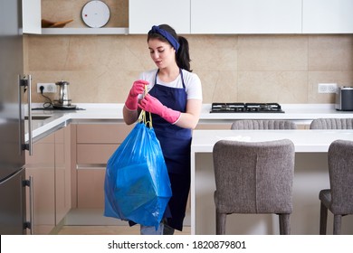 Housewife Wearing Protective Rubber Gloves Holding Garbage Bag Standing In A Kitchen. Cleaning Service Concept