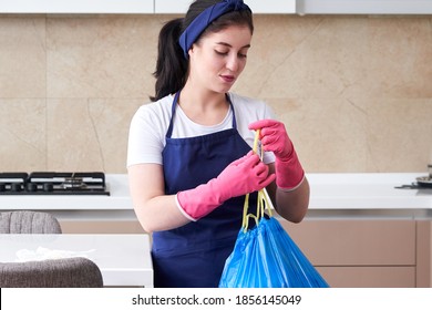 Housewife Wearing Protective Rubber Gloves Holding Garbage Bag Standing In A Kitchen. Cleaning Service Concept