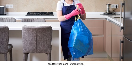 Housewife Wearing Protective Rubber Gloves Holding Garbage Bag Standing In A Kitchen. Cleaning Service Concept