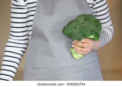 A Housewife Woman In An Apron Holds A Fresh Broccoli In Her Hand. Concept: Proper Nutrition And Weight Loss.Selective Focus