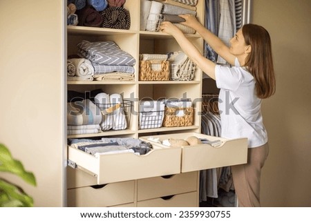 A housewife woman pulls neatly folded bed linen out of the closet. The concept of space organization and storage. Cleaning and order.