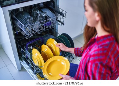 Housewife woman uses modern dishwasher for wash dishes and glasses at home kitchen