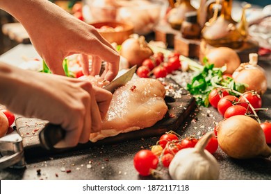 Housewife's hands cutting the fresh skinless boneless chicken breast with a knife on a wooden board.Seasoning and preparing raw chicken meat for lunch and dinner.Healthy eating, diet, lifestyle. - Powered by Shutterstock