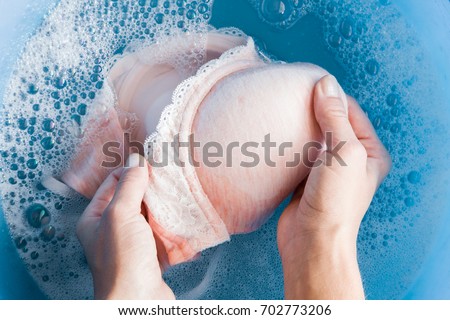 Housewife's hands washing light pink women's bra in the blue basin. Dry cleaning concept. Clothes care. Chores of maid. Regular washing. 