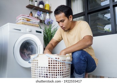 Housework. Asian Man Doing Laundry At Home Loading Clothes Into Washing Machine