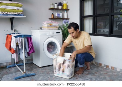 Housework. Asian Man Doing Laundry At Home Loading Clothes Into Washing Machine