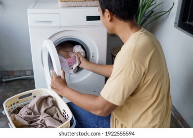 Housework. Asian Man Doing Laundry At Home Loading Clothes Into Washing Machine