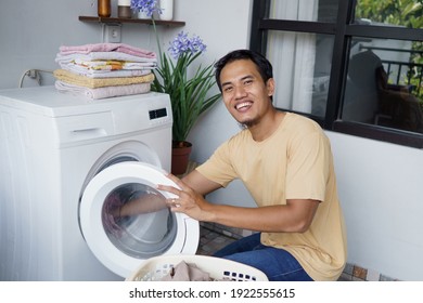 Housework. Asian Man Doing Laundry At Home Loading Clothes Into Washing Machine