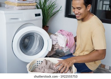 Housework. Asian Man Doing Laundry At Home Loading Clothes Into Washing Machine