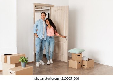 Housing Concept. Happy couple walking in empty house with cardboard carton boxes on floor, young family moving into new apartment after buying house, excited guy and lady hugging, looking around flat