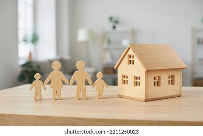 Housing for families. Close up of wooden figurines of family with children and model of small one-story house. Miniature figurines made of light wood stand on table in bright room. Blurred background. - Shutterstock ID 2211250023