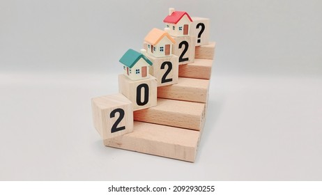 Housing and household status in 2022 being represented by stacking wooden cubes and plastic miniature houses  - Shutterstock ID 2092930255