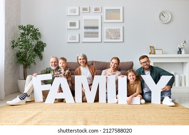 Housing and mortgage concept. Big happy family of six people grandparents, mother and father with little kids holding word FAMILY smiling at camera while sitting on floor  never sofa in   living room - Shutterstock ID 2127588020
