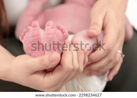 HOUSTON, TEXAS - APRIL 26TH 2023: a newborn baby’s tiny pink feet are photographed close up in their mother’s hands to compare the size. You can see every detail and line on the skin.