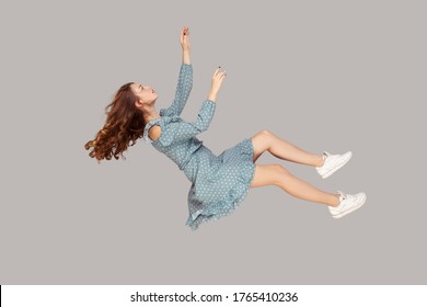 Hovering In Air. Relaxed Beautiful Girl Ruffle Dress And Curly Soaring Hair Levitating, Flying In Dream With Hands Up, Reaching For Something High. Indoor Studio Shot Isolated On Gray Background