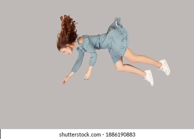 Hovering in air. Relaxed beautiful girl ruffle dress and curly soaring hair levitating, flying in dream with hands up, reaching for something high. indoor studio shot isolated on gray background
