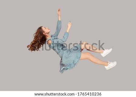 Hovering in air. Relaxed beautiful girl ruffle dress and curly soaring hair levitating, flying in dream with hands up, reaching for something high. indoor studio shot isolated on gray background