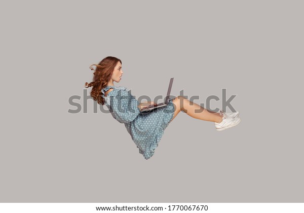 Hovering in air. Surprised girl ruffle dress\
levitating, looking at laptop screen shocked amazed, surfing web\
social networks while flying in mid-air. indoor studio shot\
isolated on gray\
background