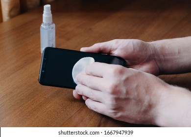 How To Clean, Sanitize Your Phone. Cleaning Mobile Phone To Eliminate Germs, Coronavirus Covid-19. Man Hands Cleaning Smartphone By Alcohol Hand Sanitizer And Wipe With Cloth.