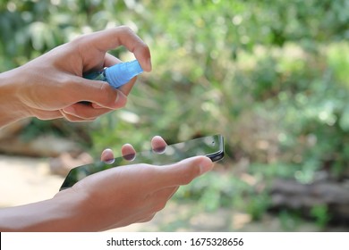 How To Clean, Sanitize Your Phone. Cleaning Mobile Phone To Eliminate Germs, Coronavirus Covid-19. Man Hands Cleaning Smartphone By Alcohol Sanitizer, Disinfectant Spray.Hygiene Concept. 