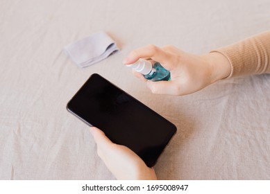 How To Clean, Sanitize Your Phone In Home. Cleaning Mobile Phone To Eliminate Germs, Coronavirus Covid-19. Man Hands Cleaning Smartphone By Disinfectant Spray.