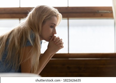How to deal with it? Side shot of thoughtful pensive sad young female sitting indoors leaning forward propping chin on clasped hands feeling desperate, unhappy, tired, lost, disappointed. Copy space