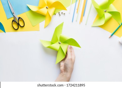 How To Make Paper Green Windmill Toy With Children At Home. Step By Step Instructions. Hands Making DIY Summer Project. Top View. Step 10. Attach Push Pin To Mark Center Of Pinwheel