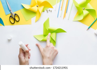 How To Make Paper Green Windmill Toy With Children At Home. Step By Step Instructions. Hands Making DIY Summer Project. Top View. Step 8. Glue Remaining Corners, Overlaying Each Other