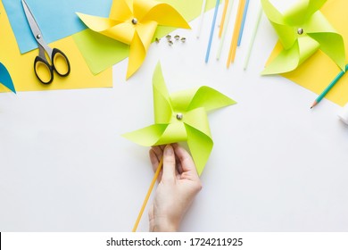 How to make paper green windmill toy with children at home. Step by step instructions. Hands making DIY summer project. Top view. Step 12. Enjoy ready pinwheel toy