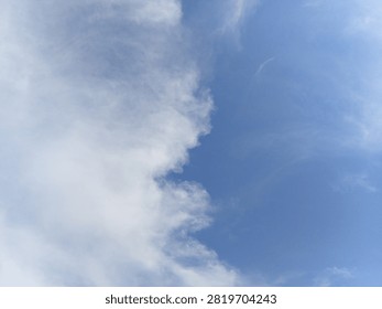 How a massive white cloud formation naturally sweeps across the bright blue daytime sky outdoors during fair weather