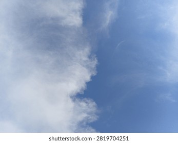 How a massive white cloud formation naturally sweeps across the bright blue daytime sky outdoors during fair weather